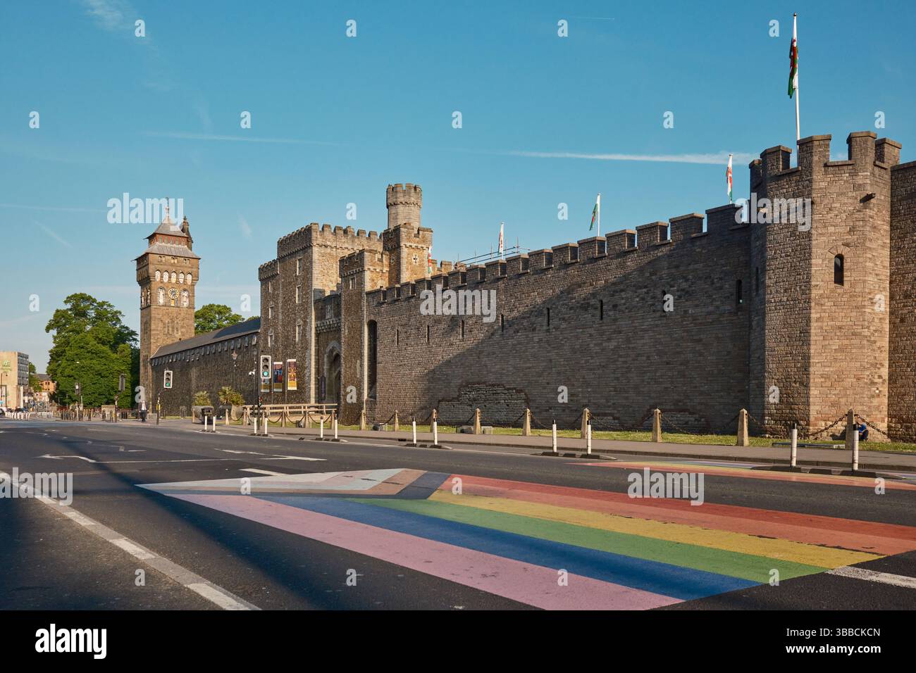 Cardiff, South Glamorgan, Regno Unito - 9 maggio 2025: Castello di Cardiff sotto un cielo azzurro. Vista ad angolo basso da Duke Street con una bandiera d'orgoglio dipinta sulla strada. Foto Stock