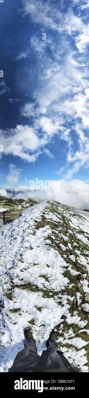 Una vista panoramica mozzafiato di un sentiero di montagna innevato sotto un vasto cielo blu adornato da soffici nuvole, catturando l'essenza del natu Foto Stock