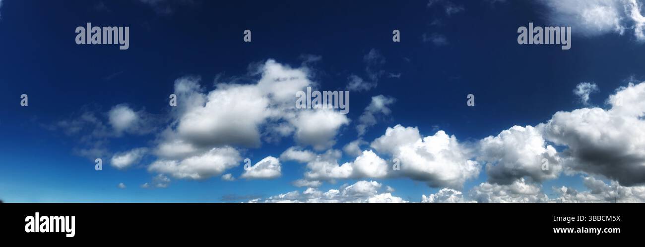Una fotografia panoramica che mostra un vasto cielo blu pieno di soffici nuvole bianche, creando un'atmosfera serena e ampia. Foto Stock