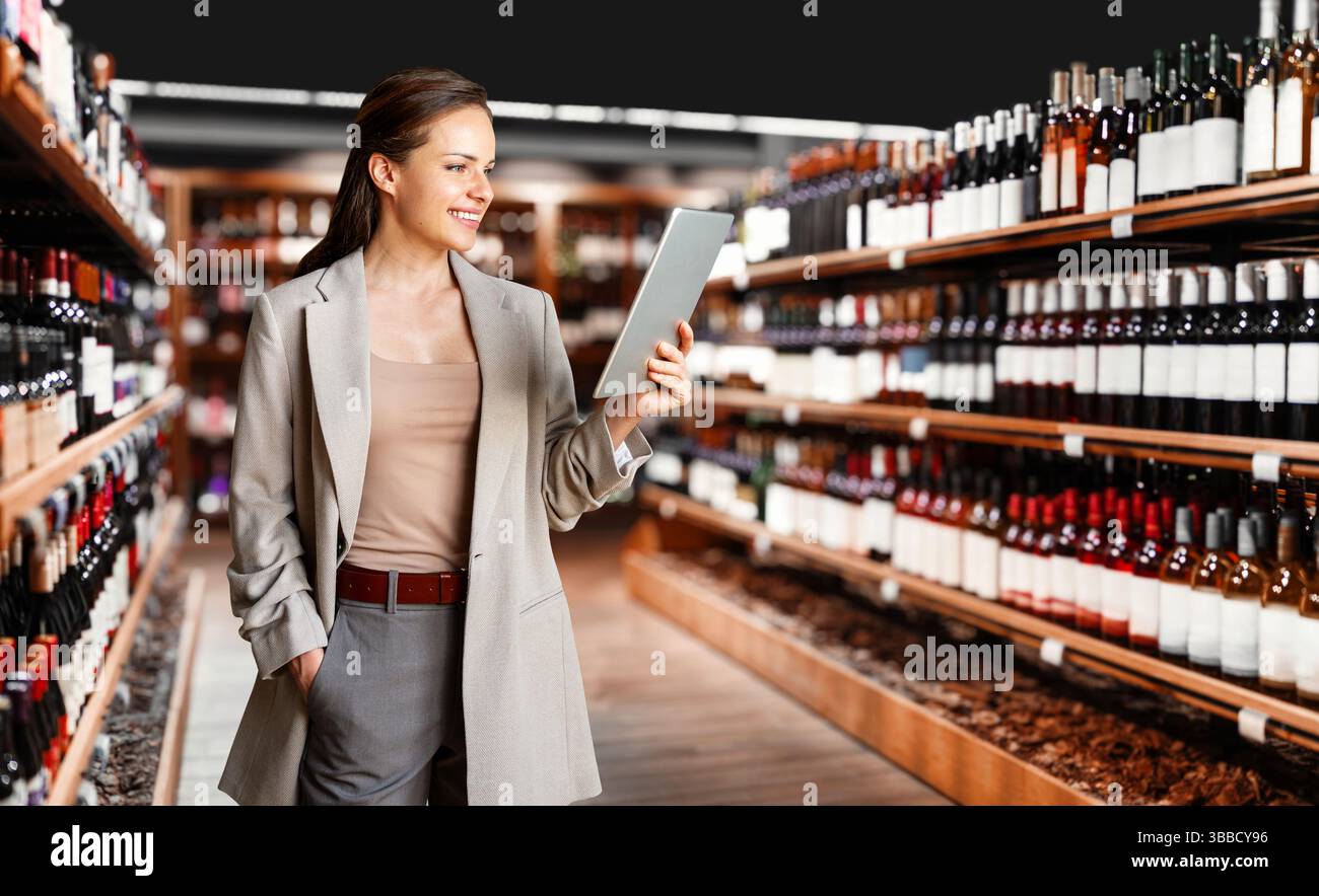 Donna d'affari sicura che utilizza un tablet digitale per gestire il negozio di liquori e analizzare i KPI del settore retail Foto Stock