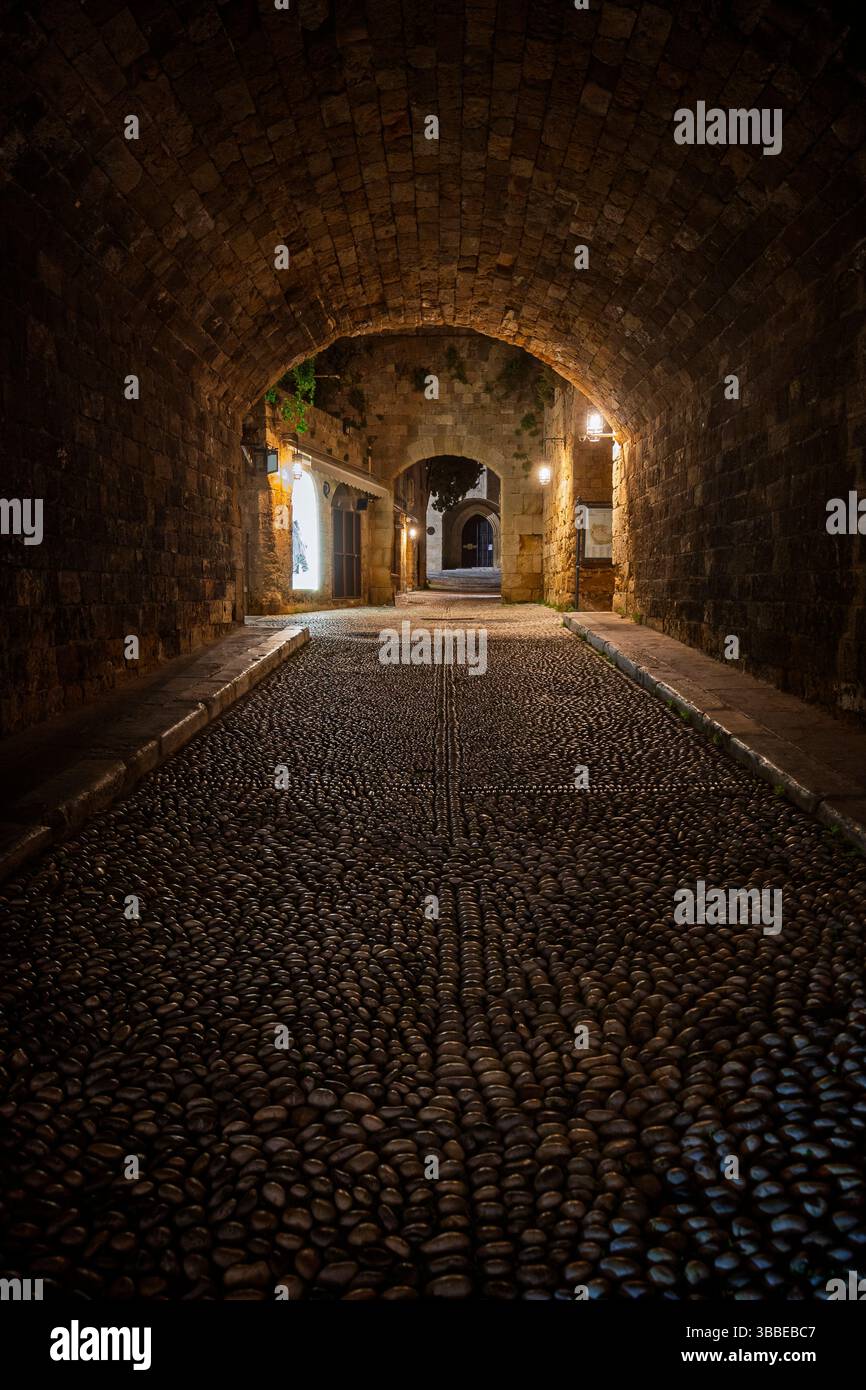 Idilliaca e vuota strada acciottolata e tunnel presso il sito medievale patrimonio dell'umanità dell'UNESCO della città vecchia di Rodi sull'isola di Rodi in Grecia di notte. Foto Stock