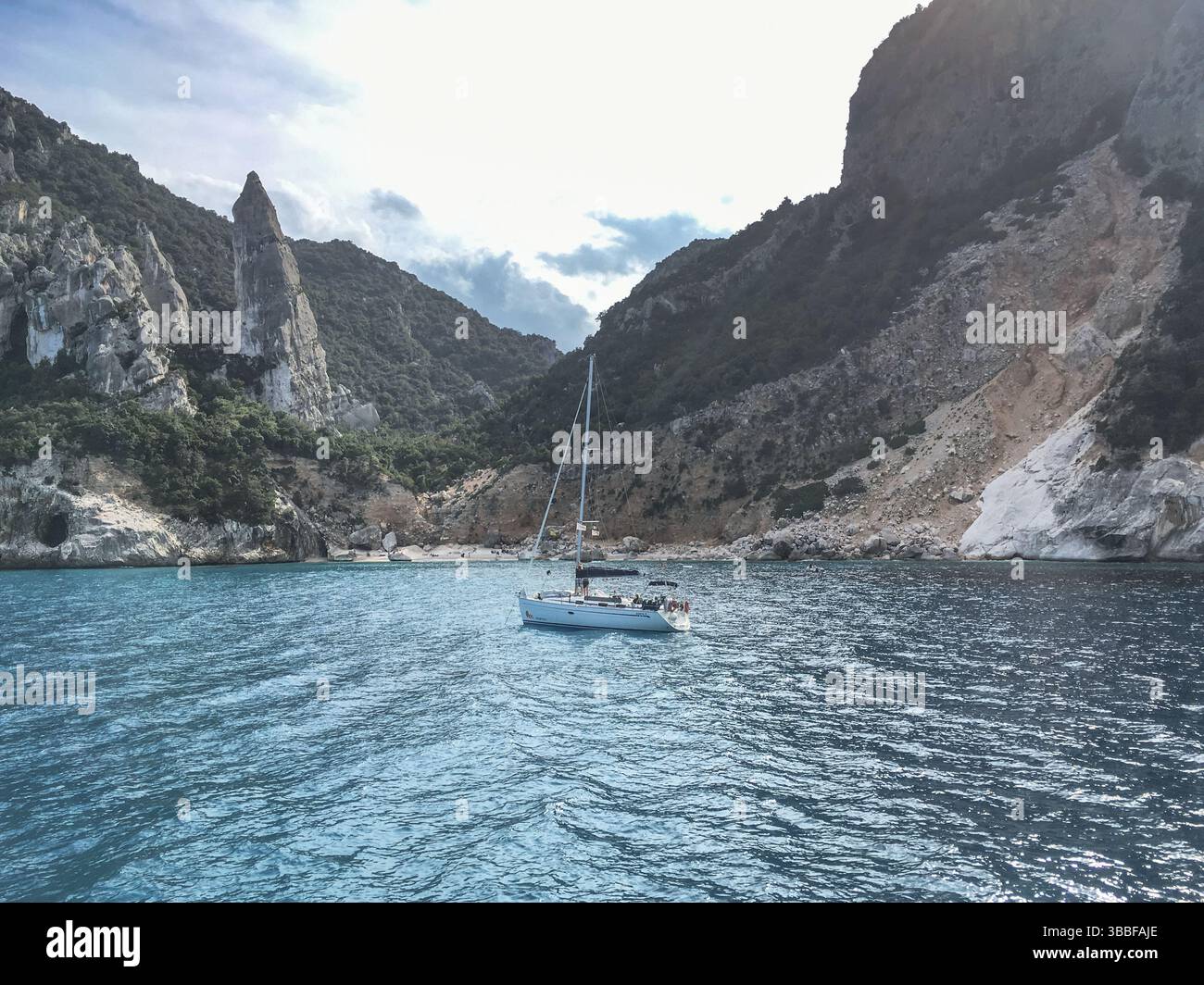 Piccola barca a vela che galleggia sul tranquillo mare turchese del mediterraneo a Costa di Baunei in Sardegna, Italia. Impressionante paesaggio roccioso di montagna sullo sfondo Foto Stock