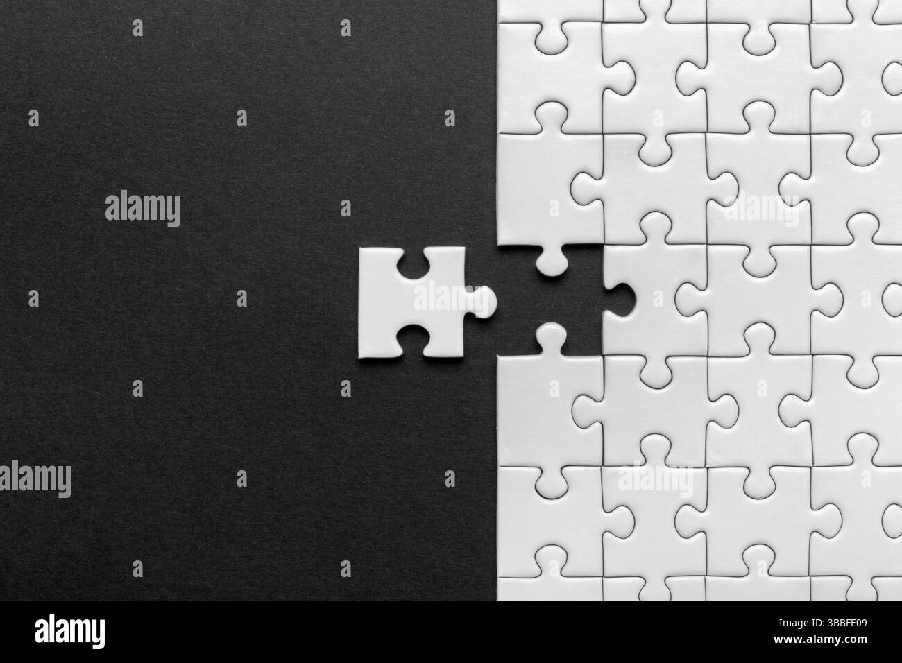 Vista dall'alto del puzzle bianco con un pezzo disallineato, su sfondo nero, contrasto bianco e nero Foto Stock