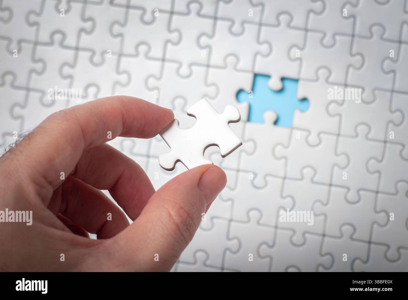 Mano che tiene il pezzo del puzzle con sfondo incompleto del puzzle Foto Stock