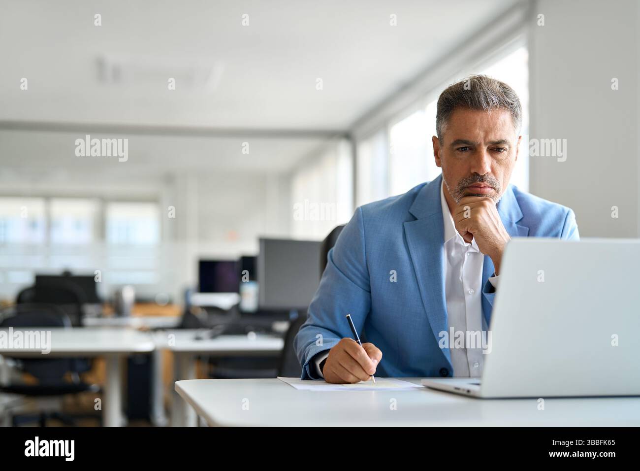 Un uomo d'affari di mezza età, serio e impegnato, che lavora su un notebook e scrive appunti in ufficio. Foto Stock