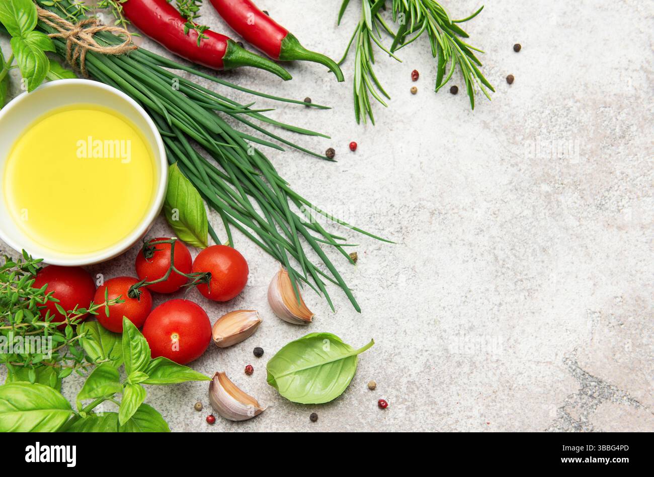Sfondo culinario con olio d'oliva, erbe fresche, spezie, pomodori ciliegini, aglio e peperoncino su sfondo grigio in cemento Foto Stock