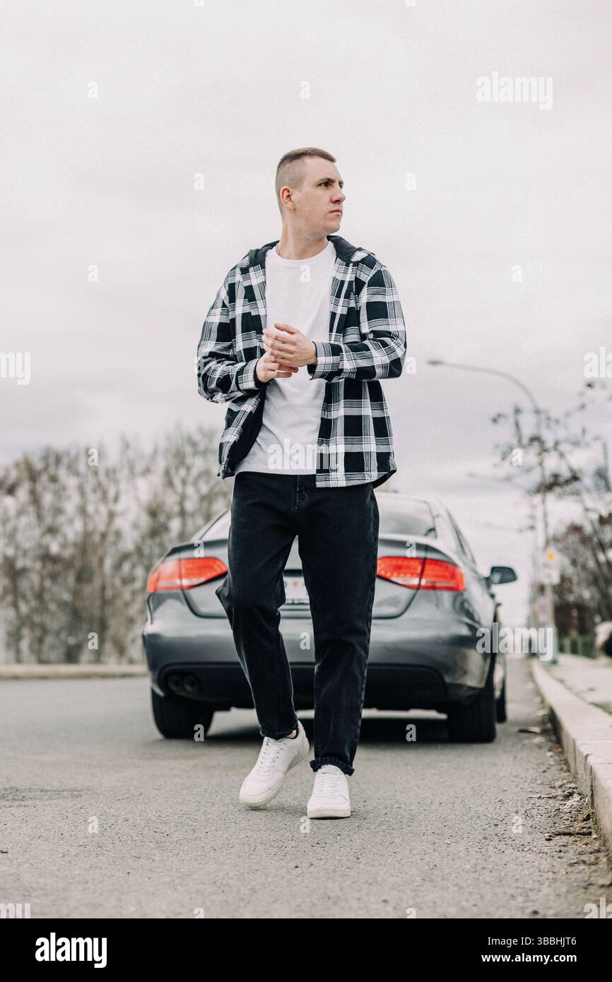 Giovane uomo che cammina con sicurezza su strada vicino alla macchina Foto Stock