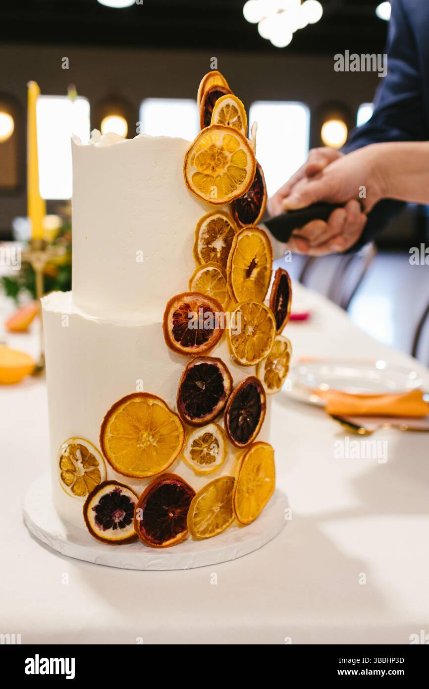 Torta nuziale bianca tagliata da sposi e sposi con dettagli agrumati Foto Stock