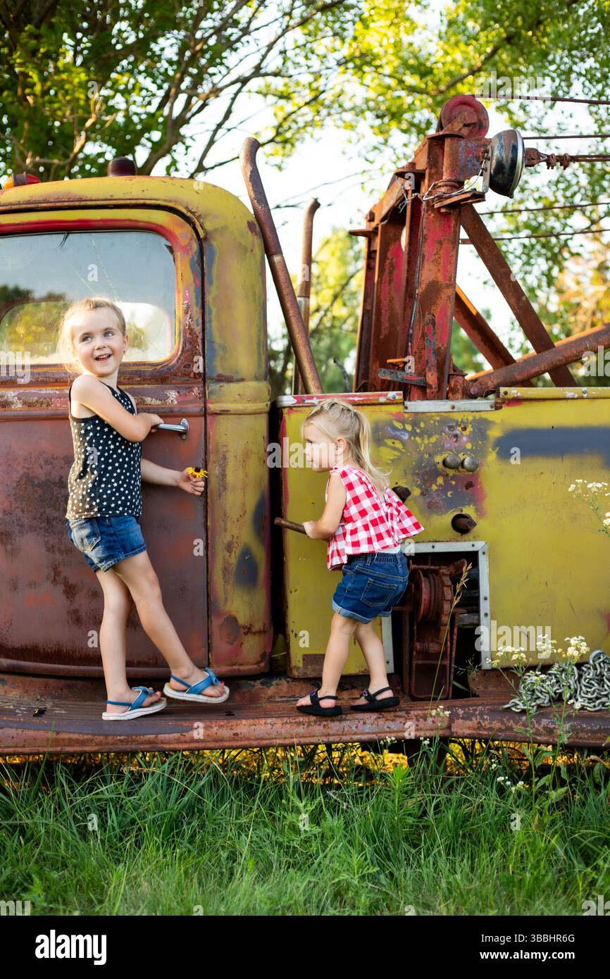 Sorelle in piedi su un antico camion giallo con fiori Foto Stock