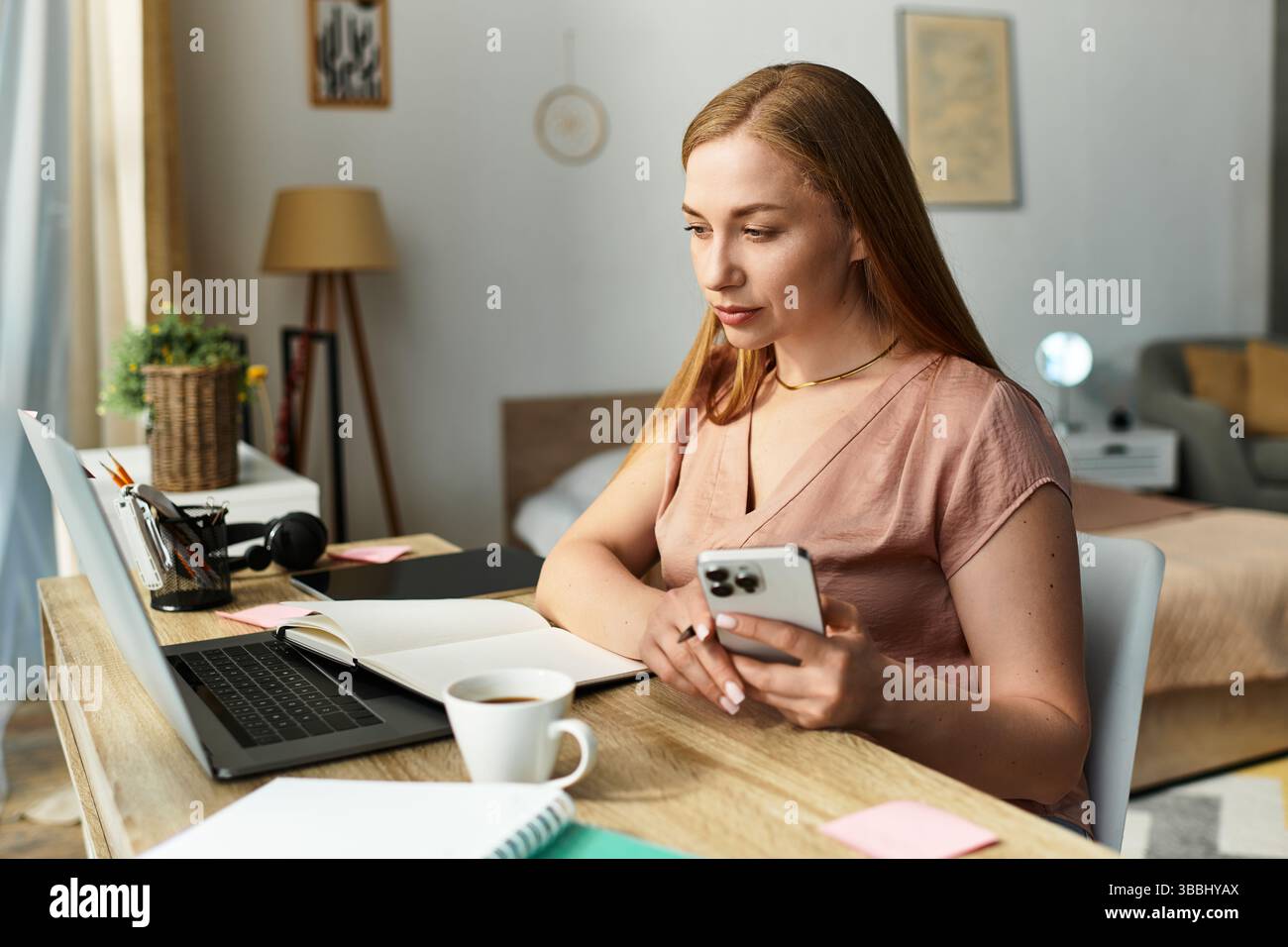 Una giovane donna siede tranquillamente alla sua scrivania, concentrandosi sulle attività con un drink caldo accanto a lei. Foto Stock