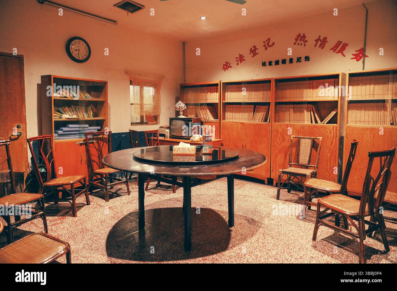 Interni dell'ufficio di registrazione delle controversie della comunità di Changsha degli anni '1980 con tavolo Lazy Susan in legno, sedie in rattan, armadi di archiviazione e TV CRT d'epoca Foto Stock