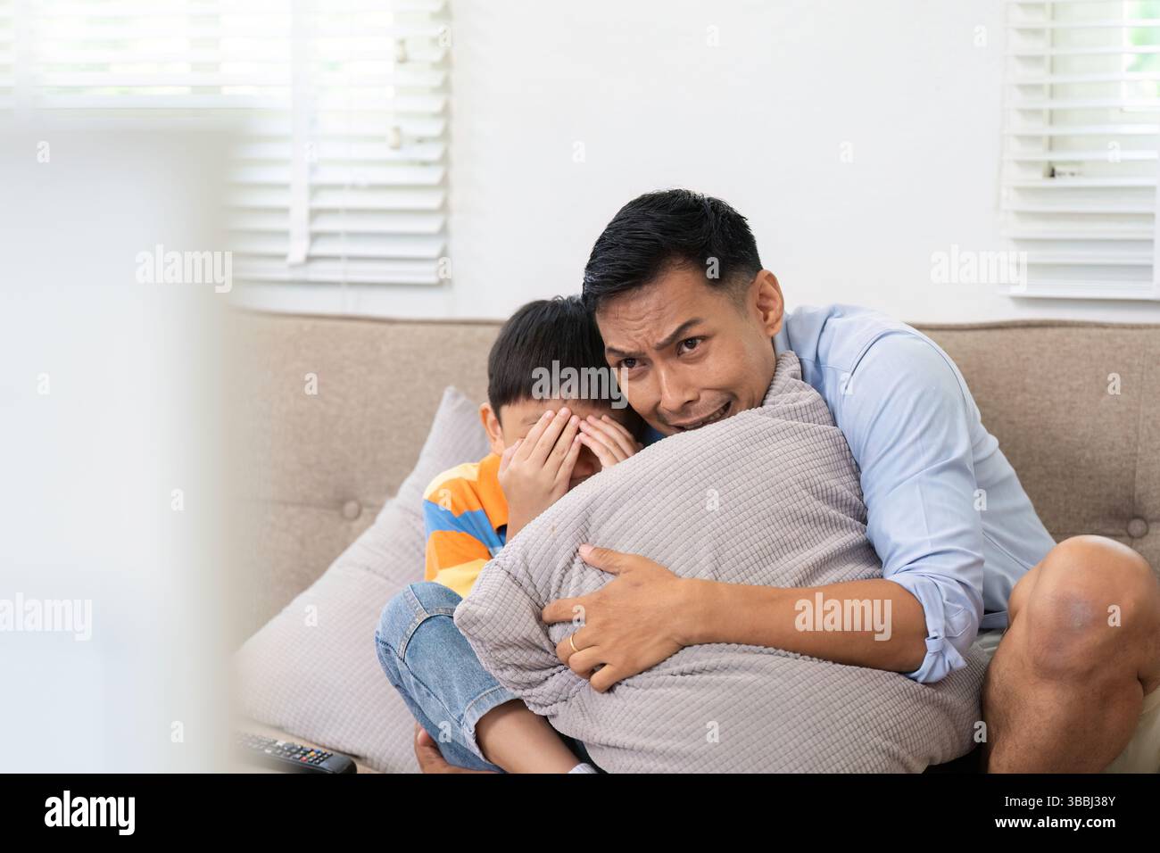 Padre e figlio che guardano un film spaventoso. Un padre conforta suo figlio durante una scena cinematografica sospettosa. Foto Stock