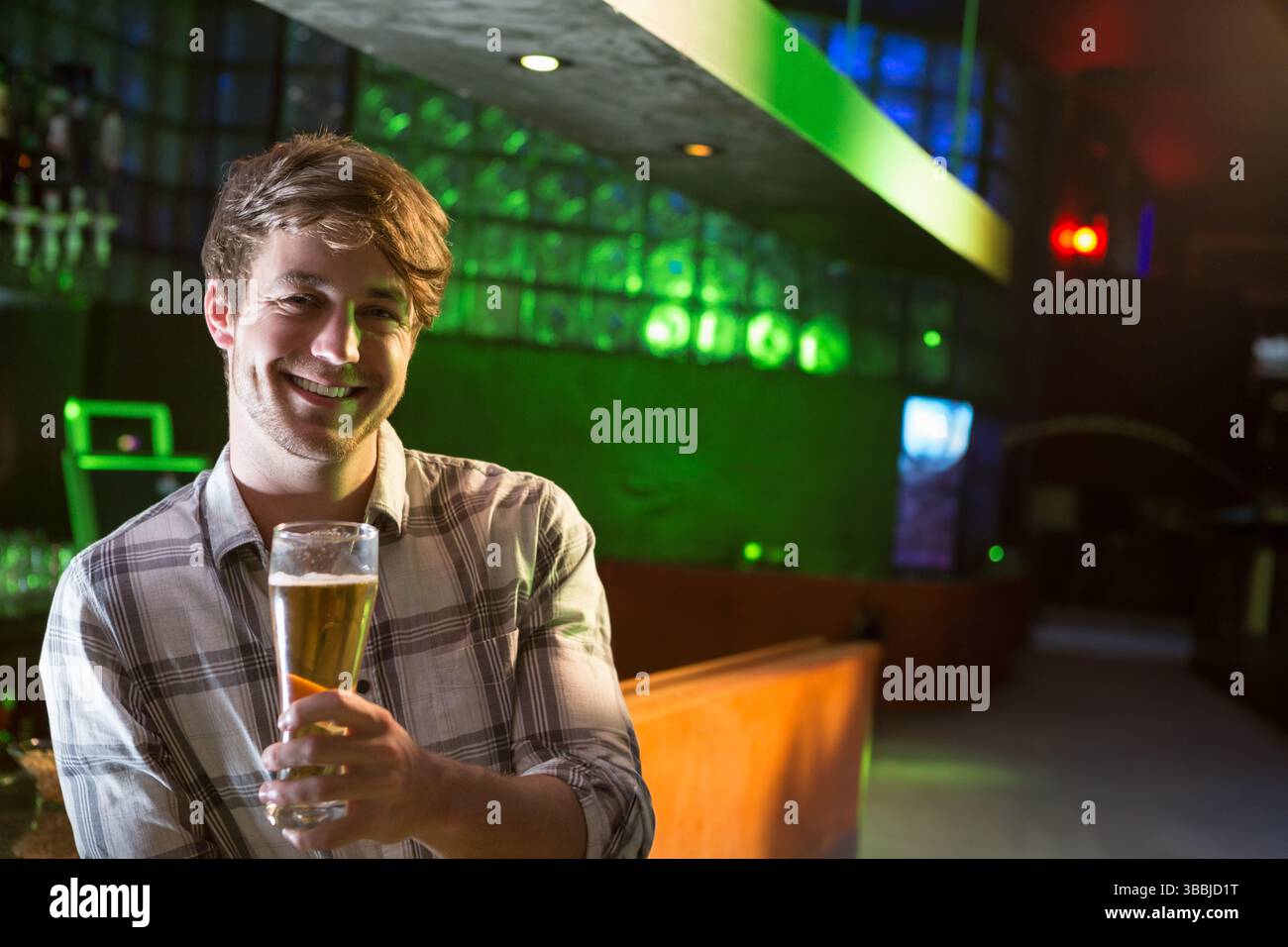 Uomo sorridente in piedi al bancone del bar del pub poco illuminato, con un bicchiere di birra alto, spazio per fotocopie Foto Stock