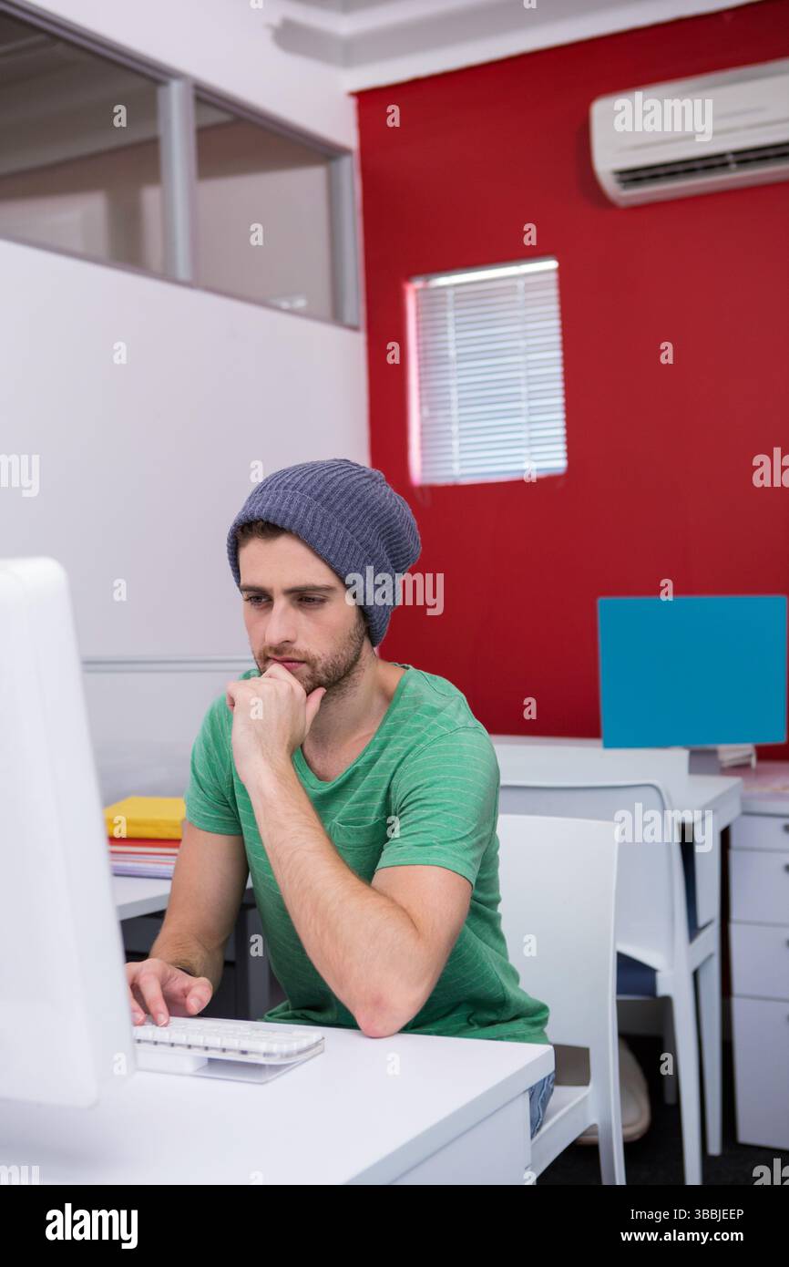 Uomo pensante di vent'anni che riposa il mento su una scrivania open space, con computer e cartelle, spazio per copiare Foto Stock