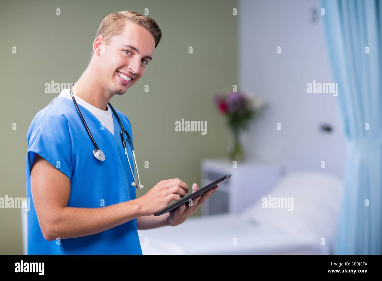Medico sorridente che tiene compresse e stetoscopio accanto al letto di ospedale nella stanza del paziente, copia spazio Foto Stock
