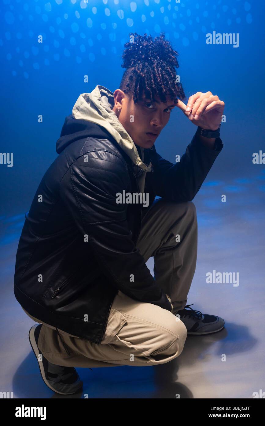 Modello afro-americano e asiatico che posa sul pavimento in uno studio con luce blu, con giacca Foto Stock