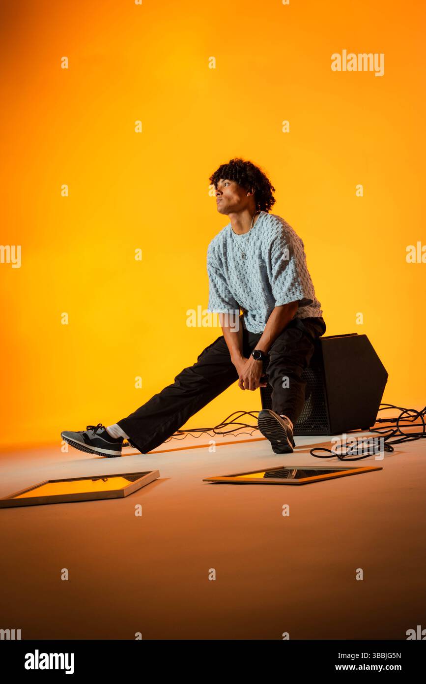 Uomo afroamericano seduto appoggiato in avanti sull'amplificatore nello studio fotografico, con cavi a spirale Foto Stock