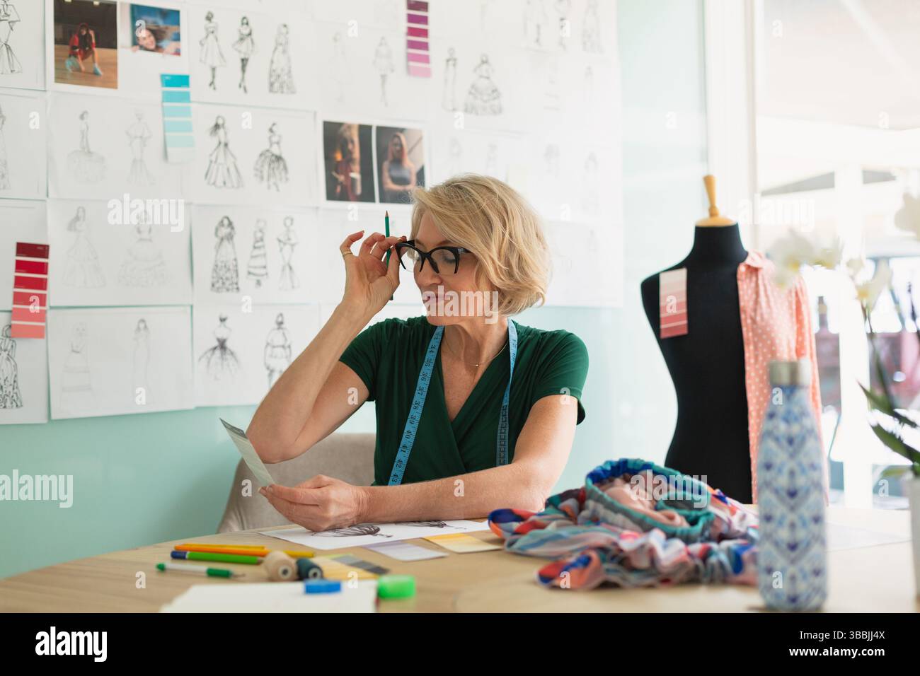 Regolazione di una donna anziana che rivede gli schizzi di carta in uno studio di design di moda, con matite colorate Foto Stock