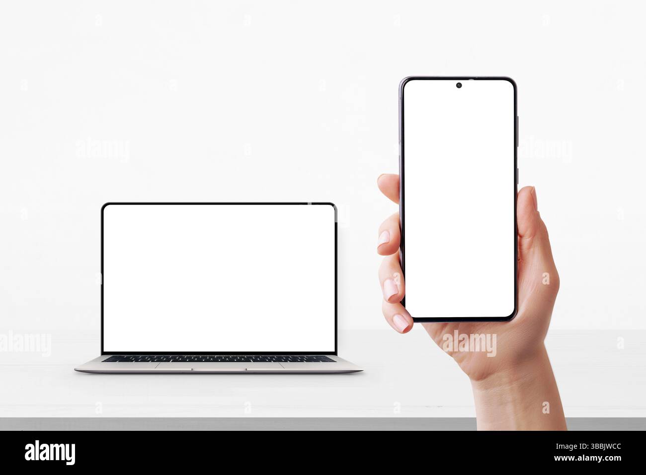 Smartphone a portata di mano con schermo vuoto e laptop in background sulla scrivania, entrambi pronti per l'interfaccia utente o il branding mockup Foto Stock