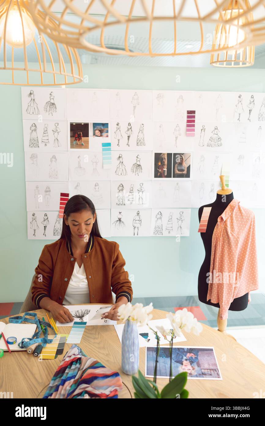 Donna che disegna disegni di moda in studio color verde menta pastello, con tavolozze di colori e forma di abito Foto Stock