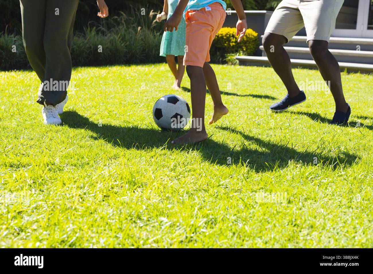 Diverse partite di calcio per tutta la famiglia sul cortile soleggiato vicino ai gradini della veranda, con pallone da calcio bianco e nero Foto Stock