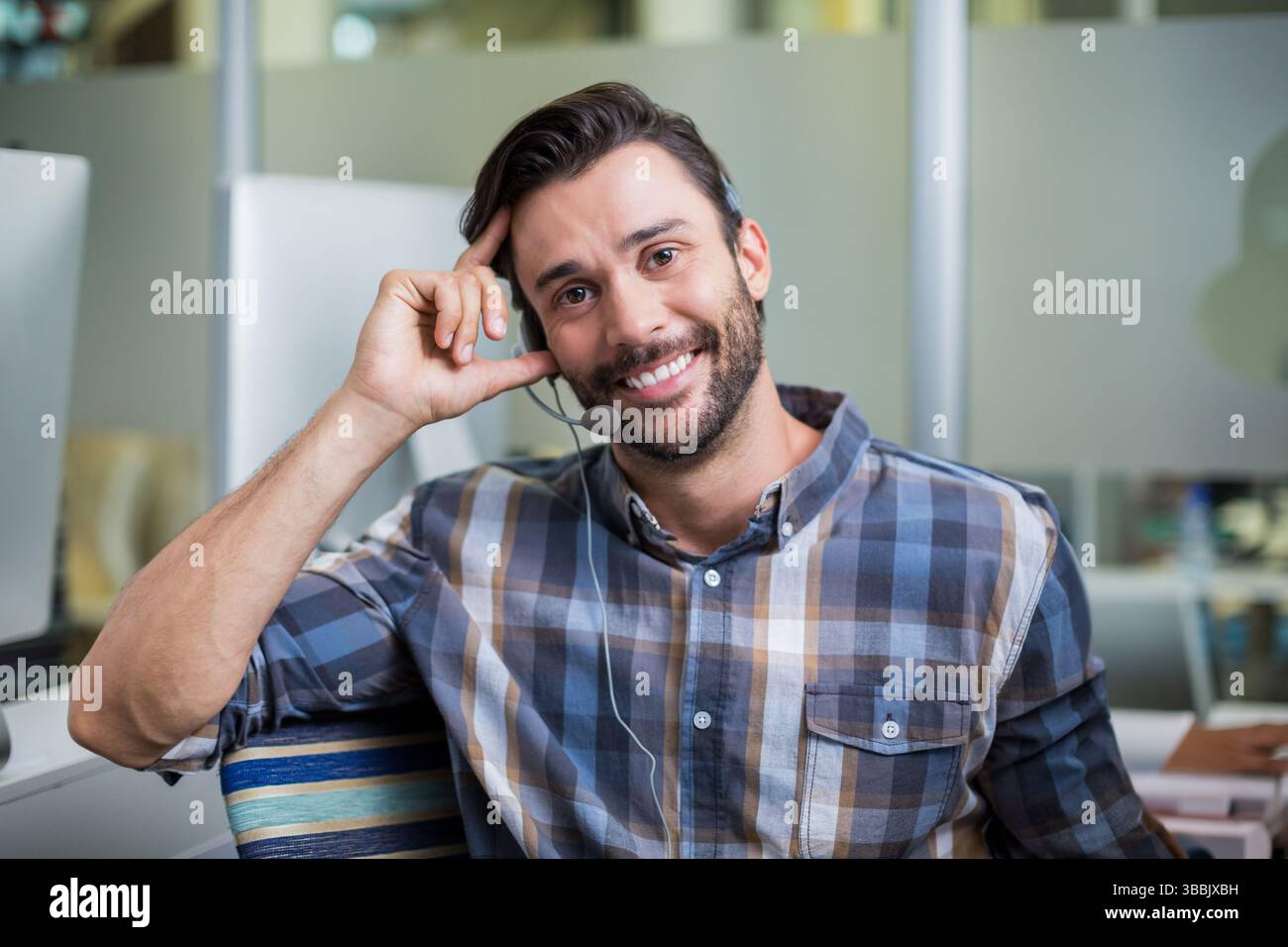 Cuffia con microfono appoggiato sulla scrivania in un ufficio open space, monitor del computer acceso Foto Stock