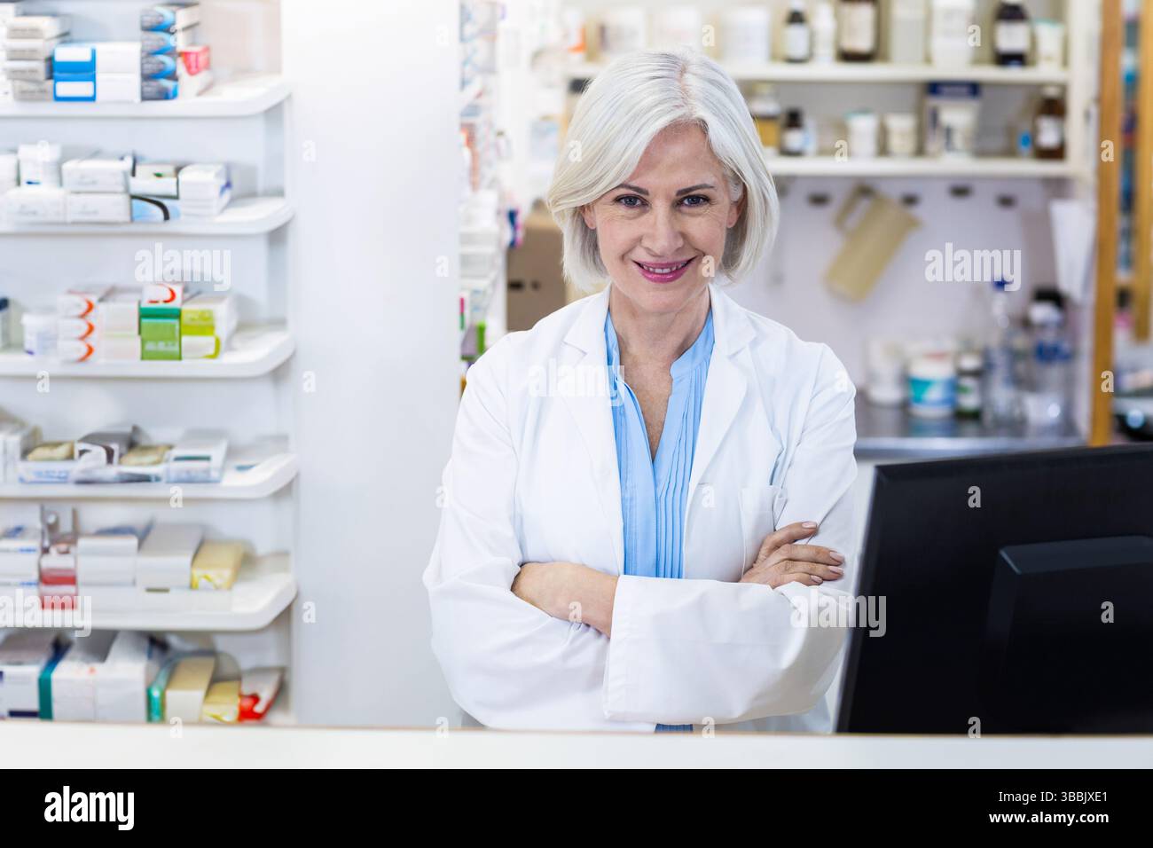 Farmacista senior sorridente in piedi dietro il bancone in farmacia, con bottiglie di farmaci Foto Stock