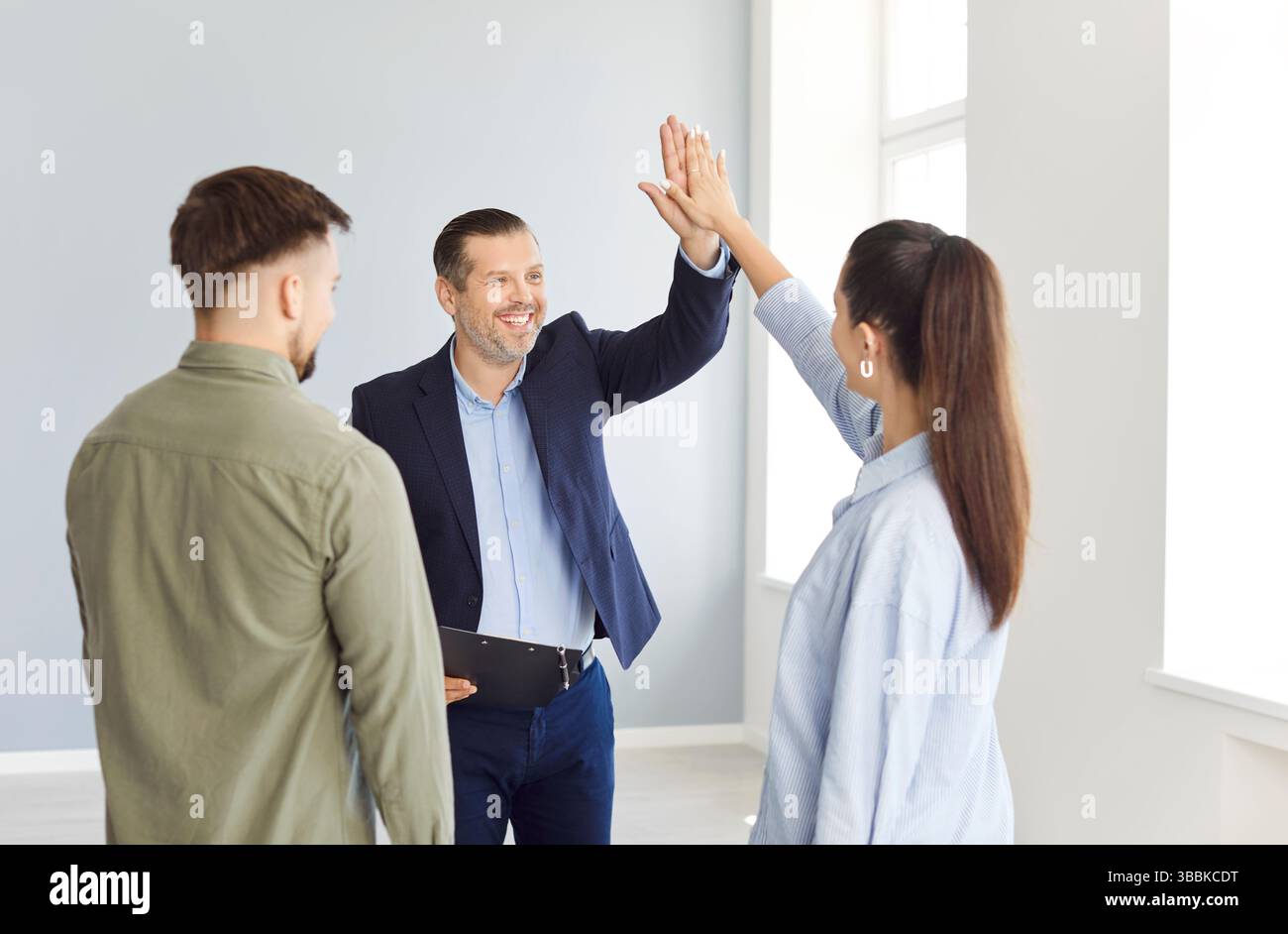 Giovane coppia High Fiving Realtor che conferma l'acquisto o il noleggio di una proprietà Foto Stock