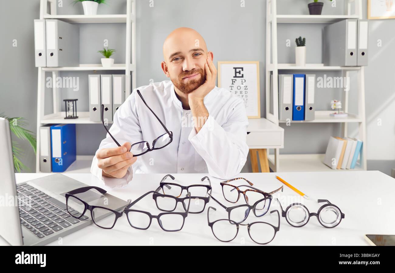 L'ottico dal volto soddisfatto offre una selezione di occhiali eleganti nel suo ufficio. Foto Stock