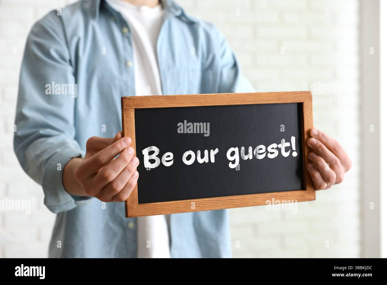Uomo che tiene una piccola lavagna con la frase Be Our Guest indoor, primo piano Foto Stock