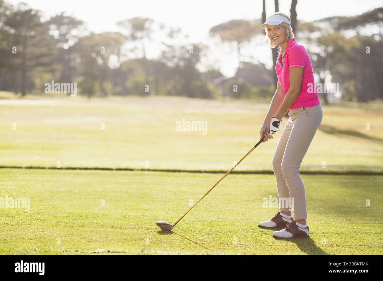 Donna in piedi che tiene il conducente sul tee box, indossa una visiera, con palla da golf e spazio per copiare Foto Stock