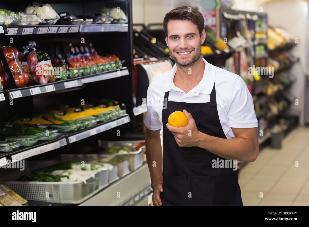 Lavoratore sorridente del negozio di alimentari che tiene l'arancia nella corsia dei prodotti, con frutta confezionata, spazio per copie Foto Stock