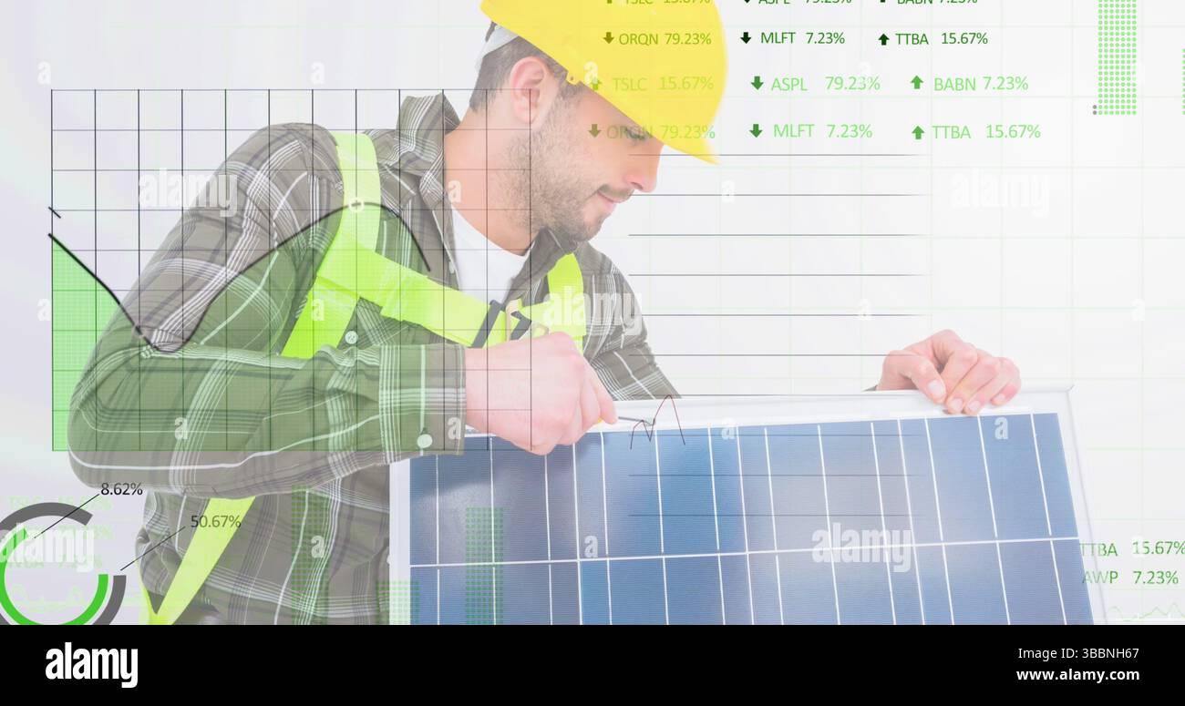 Uomo che indossa elmetto giallo, giubbotto di sicurezza che regola il pannello solare in studio, con grafici finanziari Foto Stock