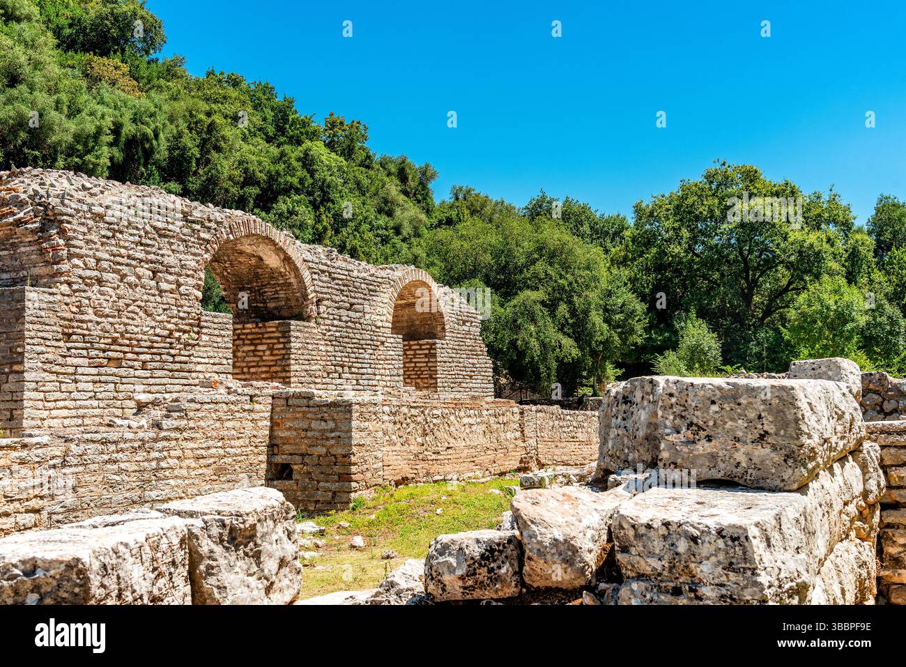 Due archi a botte romane che si innalzano sopra blocchi calcarei intemprati a Butrint incorniciati da lussureggianti boschi mediterranei e da un cielo estivo limpido Foto Stock
