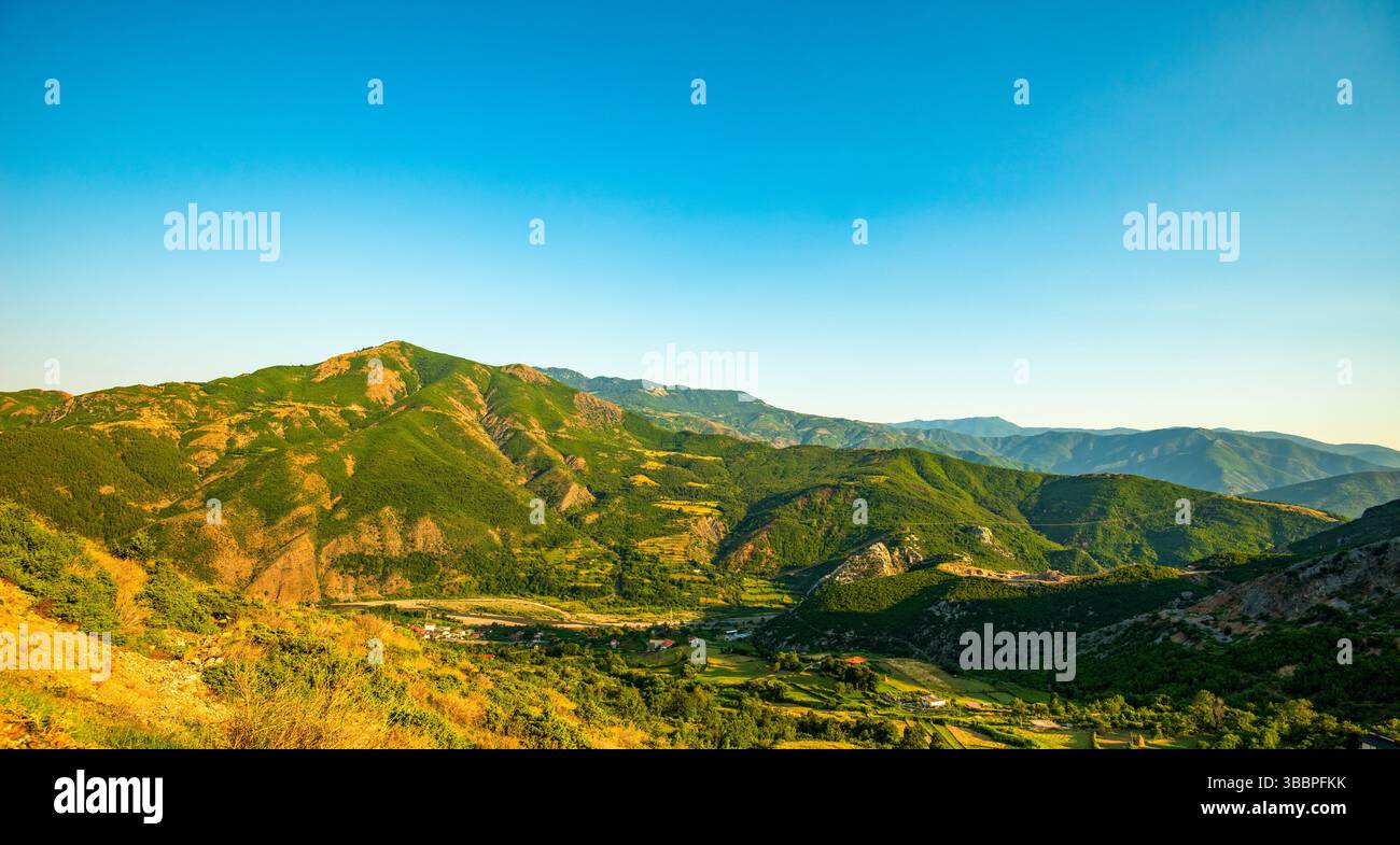 vista panoramica di Rruga Egnatia (via Egnatia) che si snoda tra verdeggianti vallate di montagna e terreni agricoli terrazzati sotto un cielo azzurro e limpido albanese Foto Stock