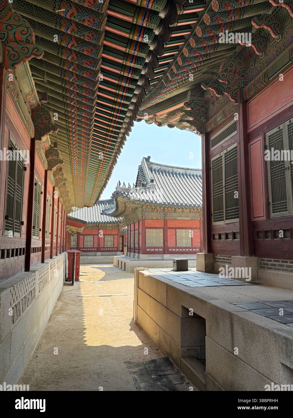 Le grondaie decorate con il dancheong fiancheggiano un tranquillo corridoio di palazzo a Seoul, Corea, un testamento della simmetria, dell'arte e della tradizione reale - Immagine stock catturata con smartphone