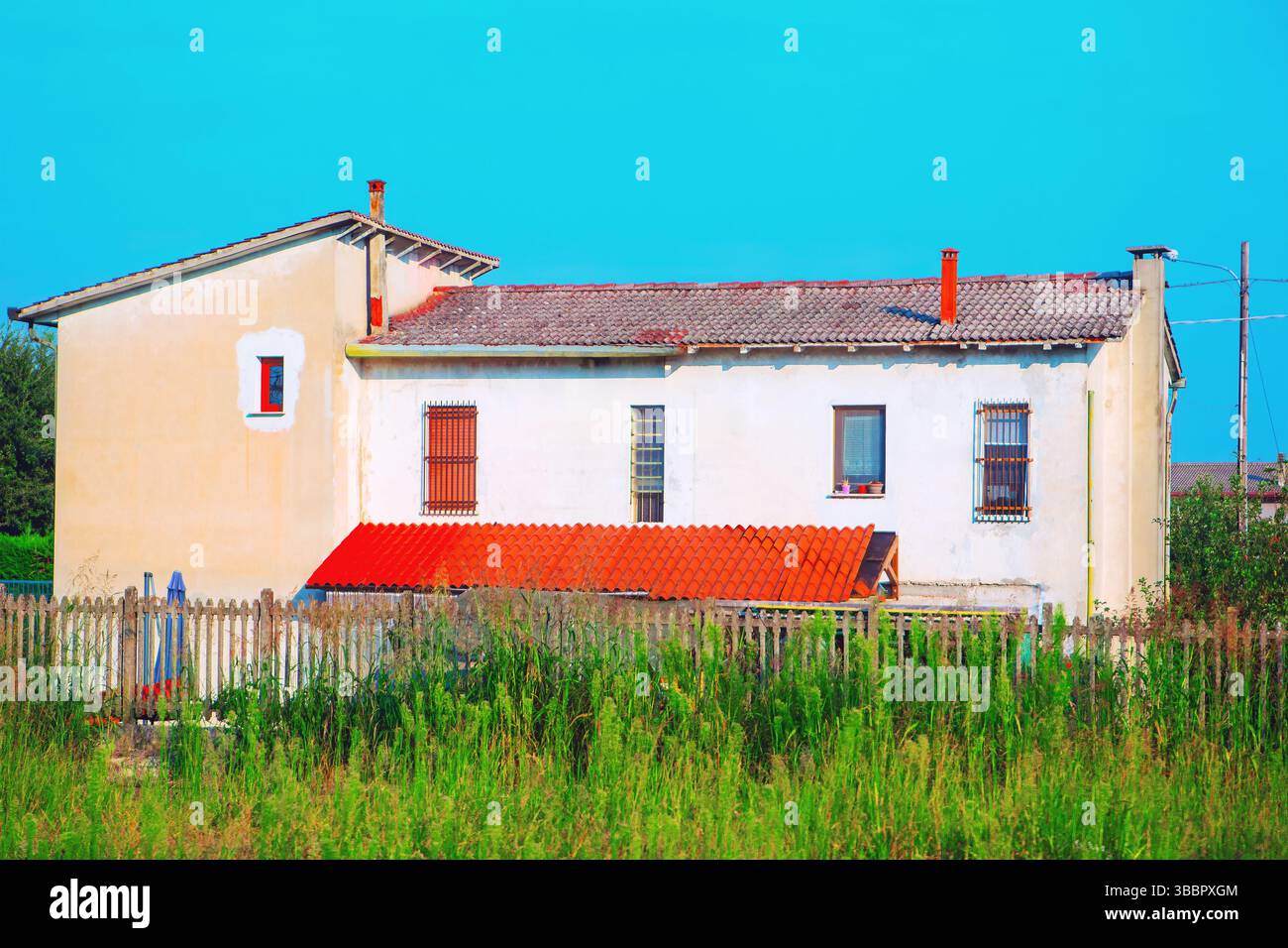 Tranquillo scenario rurale, caratterizzato da una casa con tetto piastrellato rosso, annidata dietro una semplice recinzione di legno e erba ricoperta Foto Stock