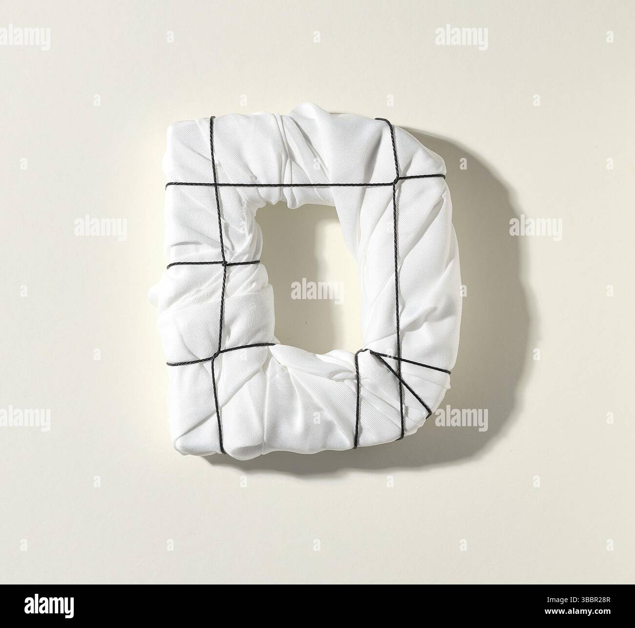 Lettera D rivestita in tessuto bianco con cordoncino nero su sfondo beige, vista dall'alto Foto Stock