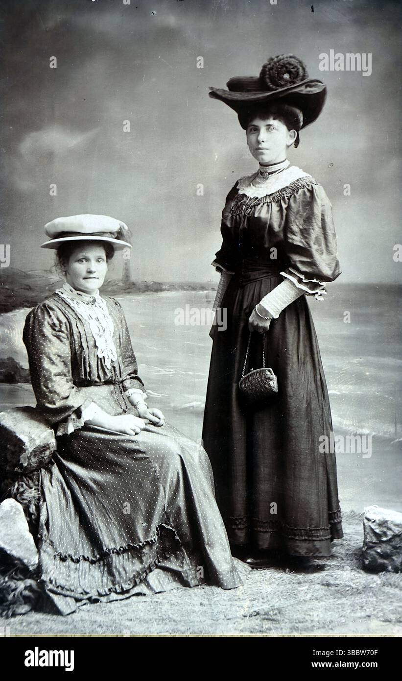 Storia sociale, moda: Due signore, una in piedi, l'altra seduta. Entrambi indossano gonne lunghe o abiti, cappelli, e la donna in piedi ha una piccola borsa. Non attribuito, intorno al 1910. Da una collezione mista di cartoline edoardiane. Foto Stock