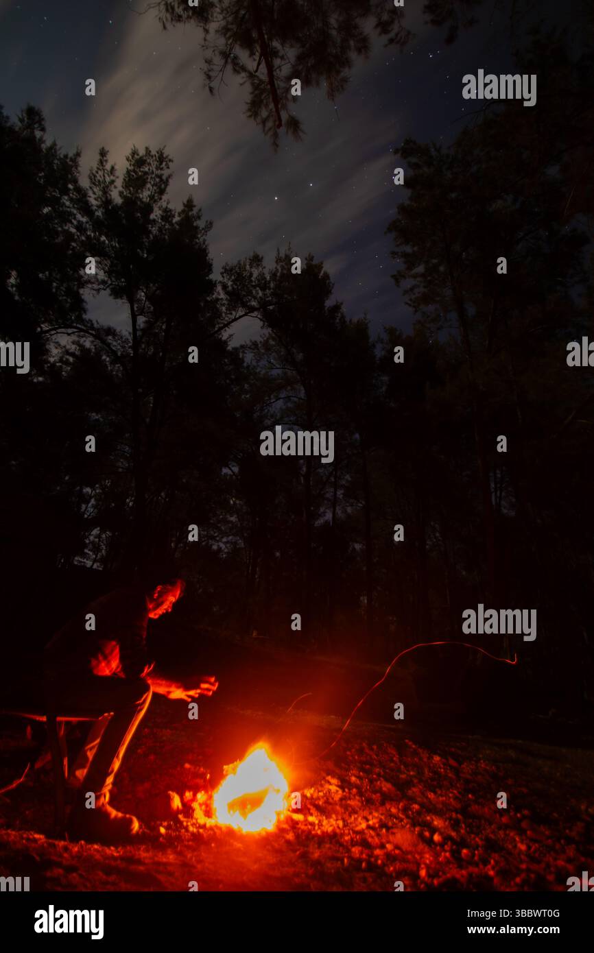 Riscaldare le mani da un fuoco sotto le stelle nel Bush australiano Foto Stock