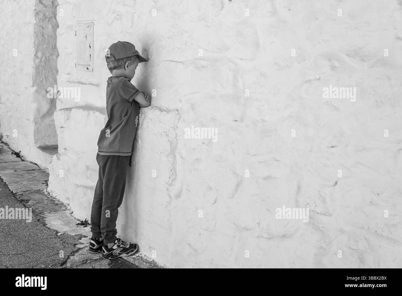 Huffed boy resta di fronte al muro bianco Foto Stock