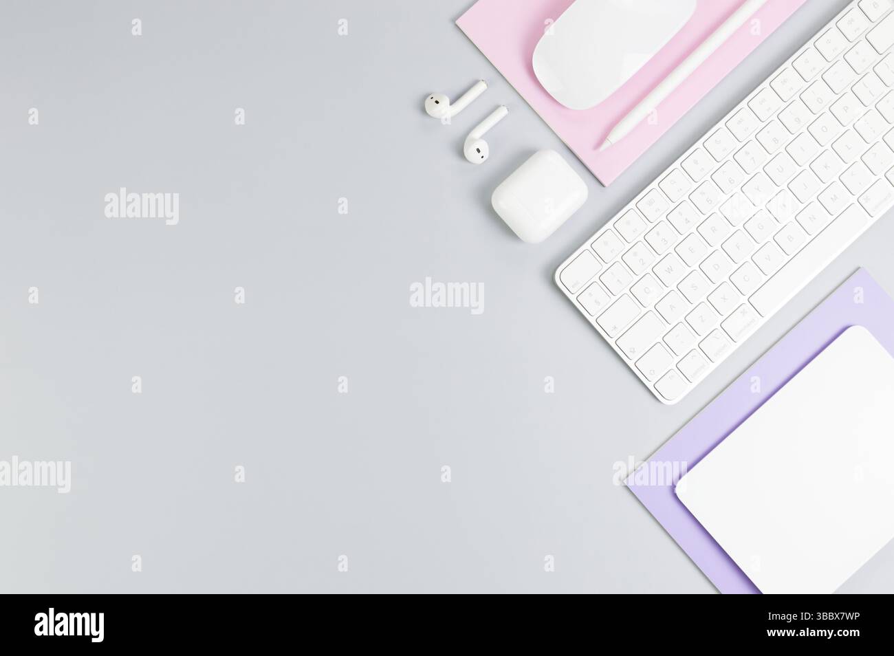 Vista dall'alto di tastiera bianca, mouse, touchpad, custodia per auricolari, penna su sfondo grigio. Quaderni viola e rosa, ufficio moderno, scuola. Foto Stock