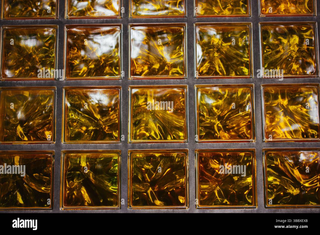 Parete in vetro dorato che mostra una texture unica Un primo piano di una parete in vetro, con una vibrante tonalità dorata. I blocchi di vetro quadrati nel bagno Foto Stock