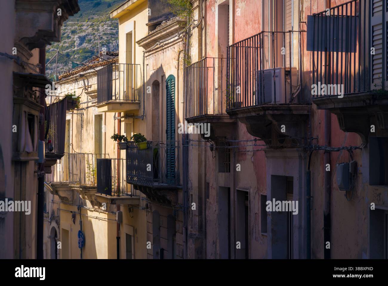 La luce del sole proietta ombre morbide su edifici colorati con balconi ornati a Ragusa, creando un'atmosfera serena al crepuscolo, Sicilia, Italia Foto Stock