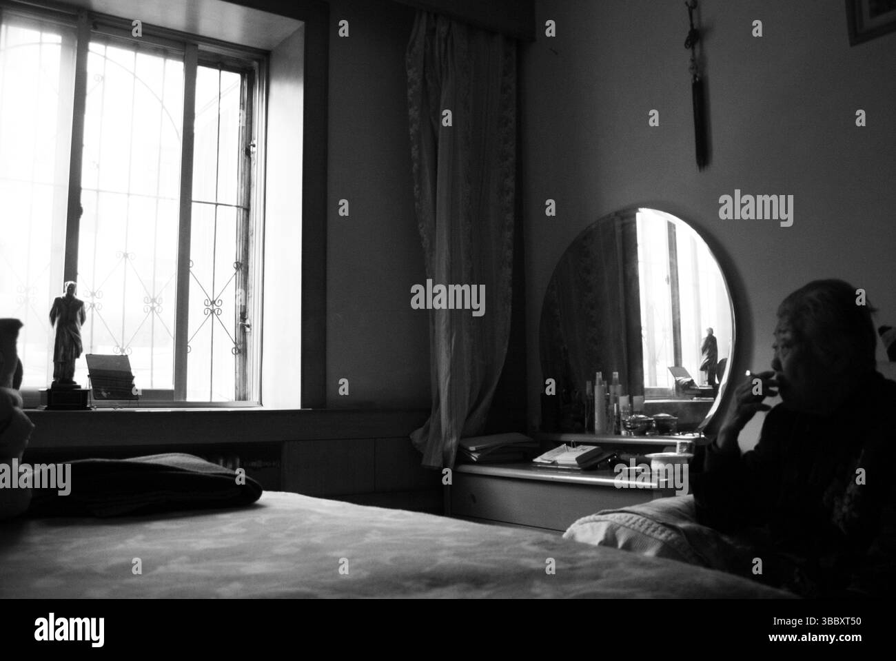 Fumo e memoria: Anziana donna cinese guarda la statua di Mao Zedong in camera da letto Foto Stock