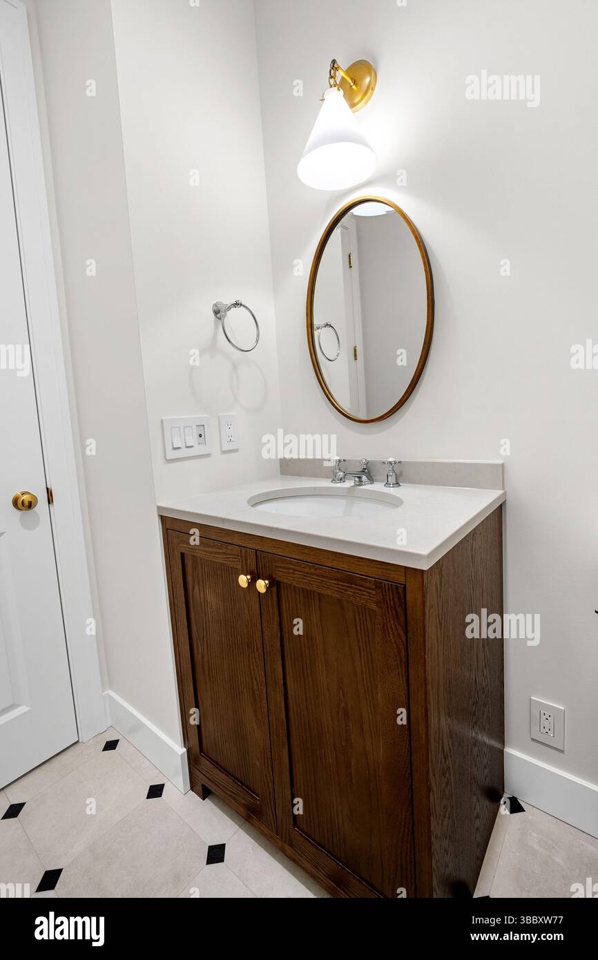 Piccolo mobile da bagno con fronte in legno sotto uno specchio rotondo e una lampada da parete. Foto Stock