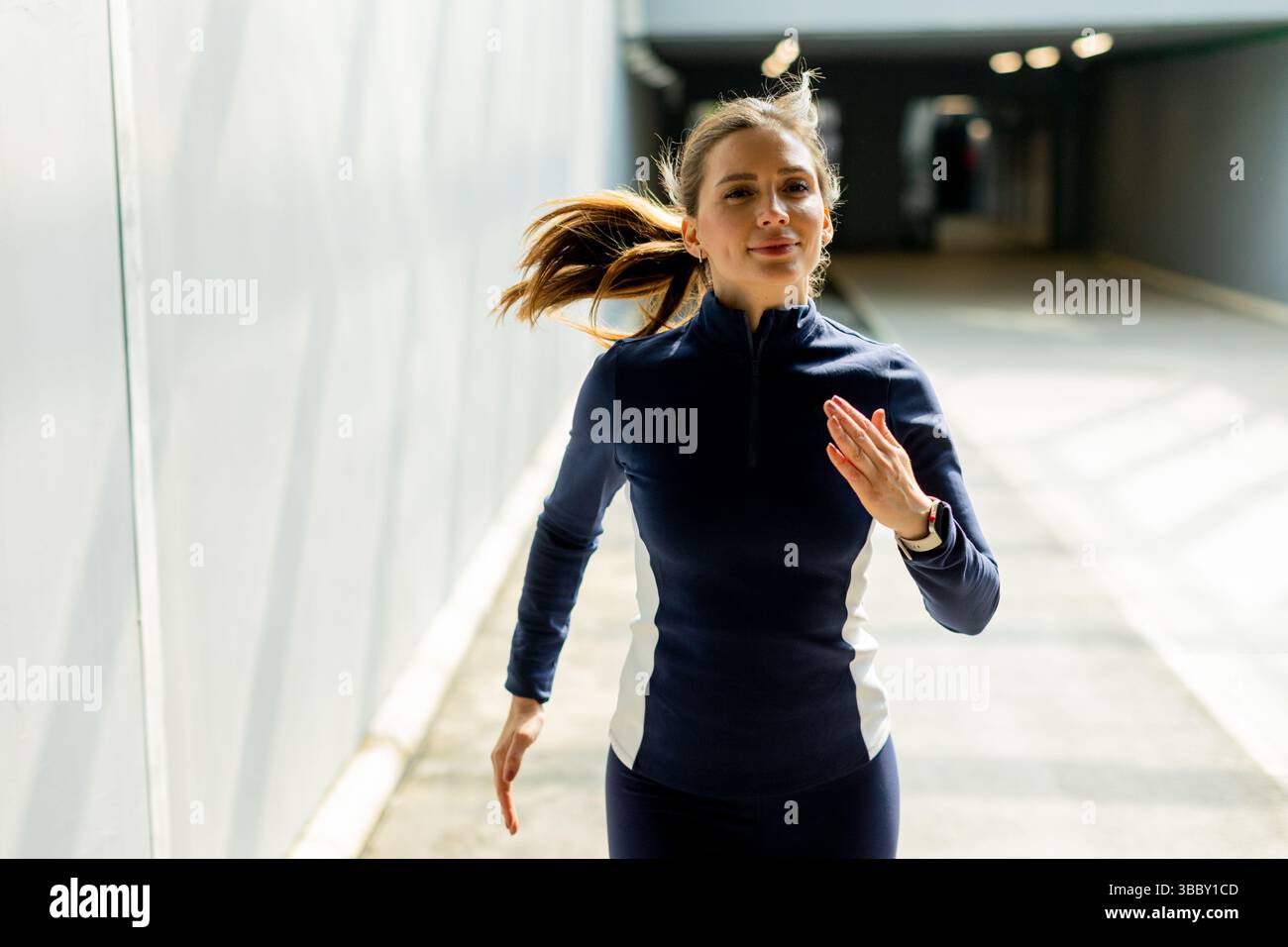 Una donna di abbigliamento sportivo ama correre attraverso un passaggio elegante e contemporaneo, abbracciando l'aria fresca del mattino e la vibrante energia. Foto Stock