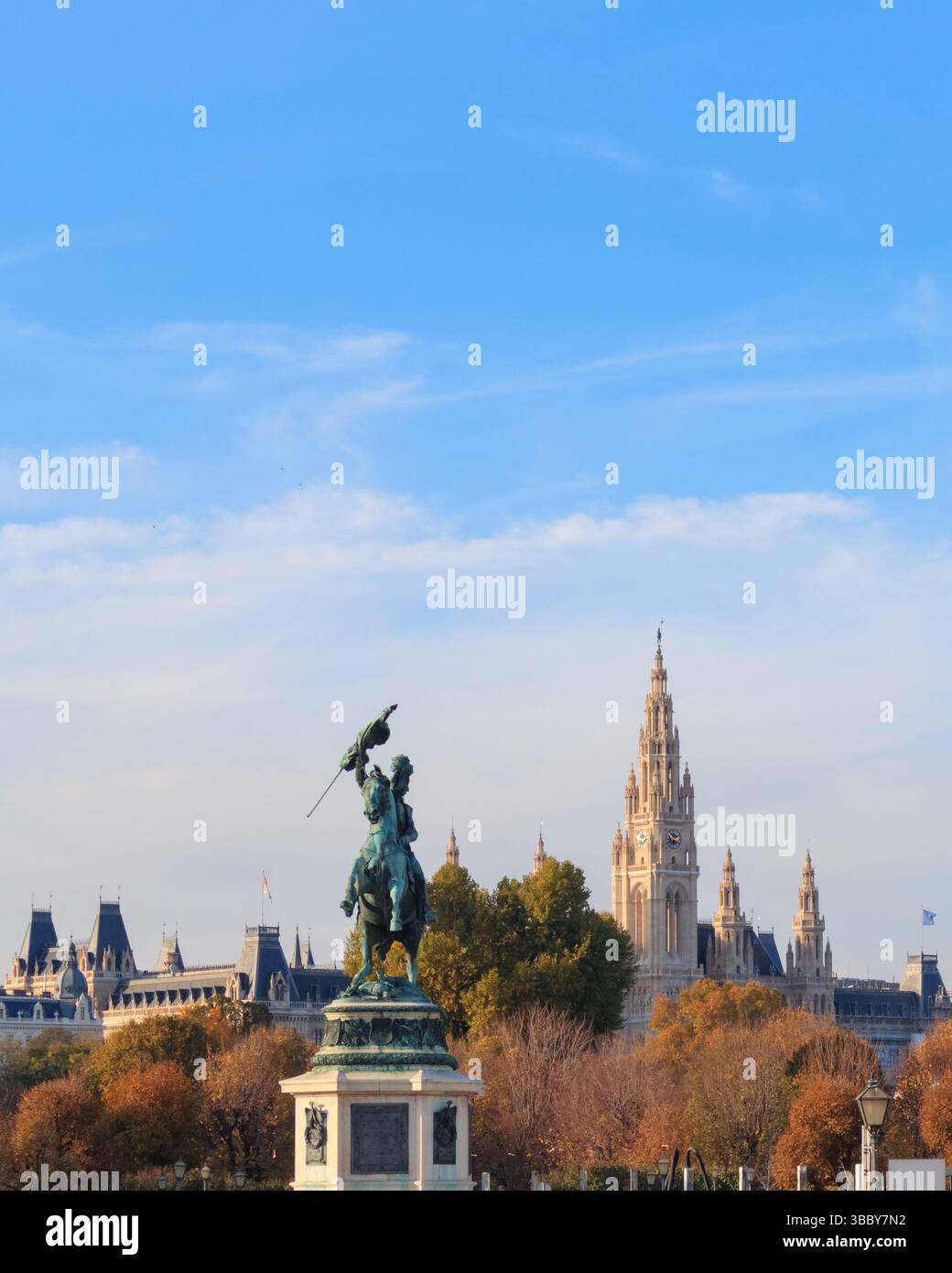 Un'impressionante statua in bronzo si erge in primo piano contro lo skyline di Vienna, che mostra la bellezza architettonica con alberi adornati con colori autunnali Foto Stock