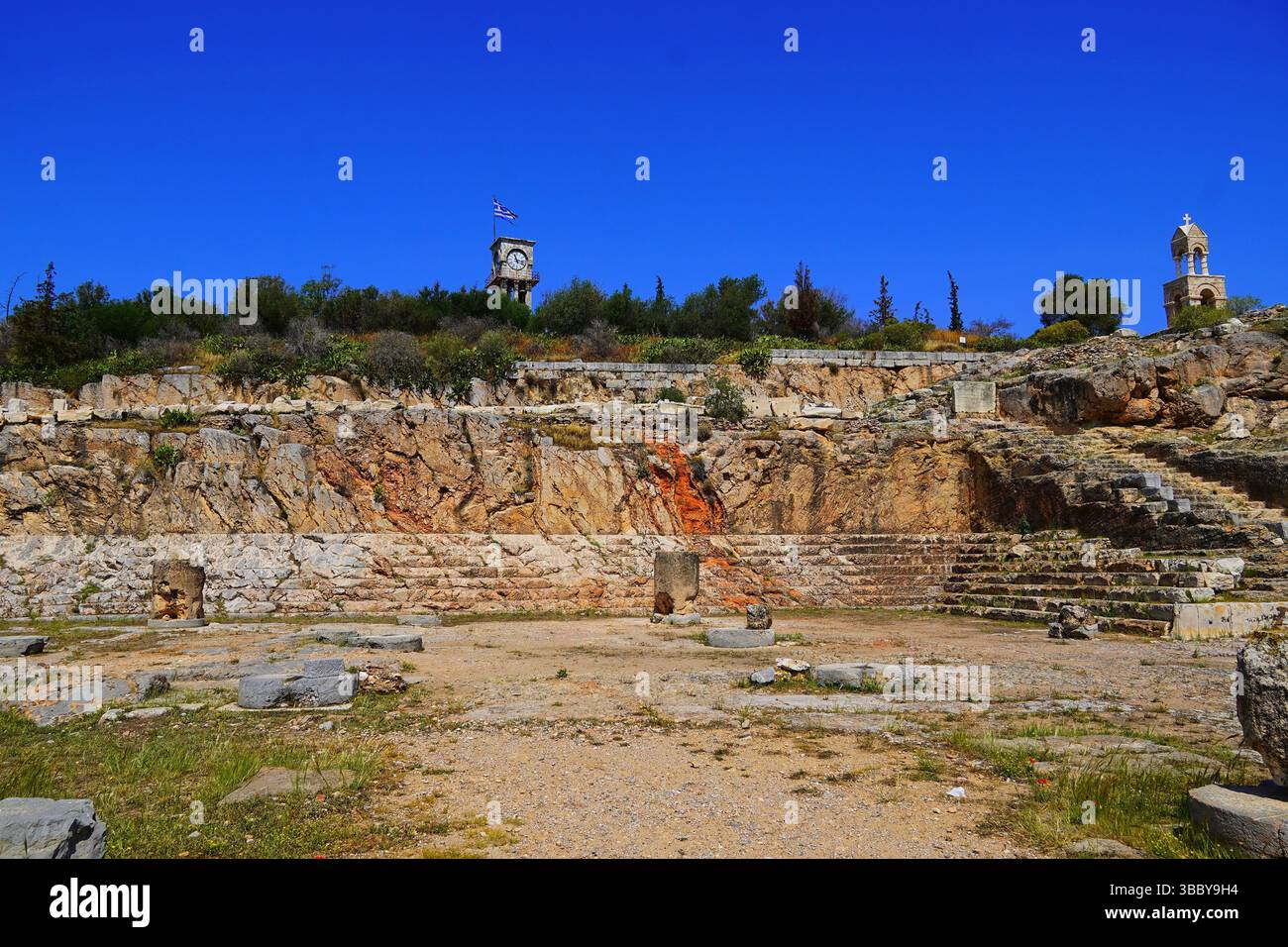 Vista dell'antico edificio scolpito della cerimonia di culto, il Telesterion, una piccola chiesa cristiana e una torre dell'orologio, a Eleusi o Elefsina, in Grecia Foto Stock