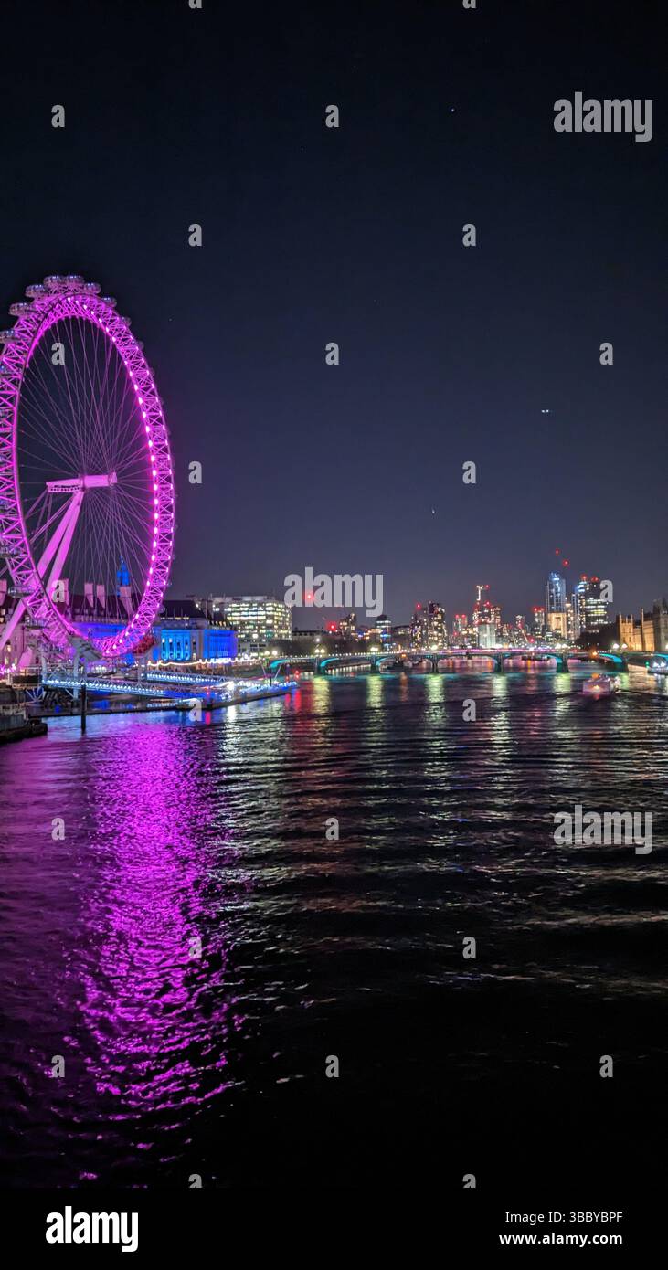 Una vibrante vista notturna del London Eye illuminata di sfumature rosa e viola, che si riflette sul fiume Tamigi. - Immagine stock catturata con smartphone